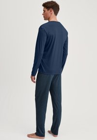 Schwarzes Langarmoberteil mit rundem Halsausschnitt, kombiniert mit gemusterten Schlafanzughosen in Dunkelblau, die ein geometrisches Design aufweisen.