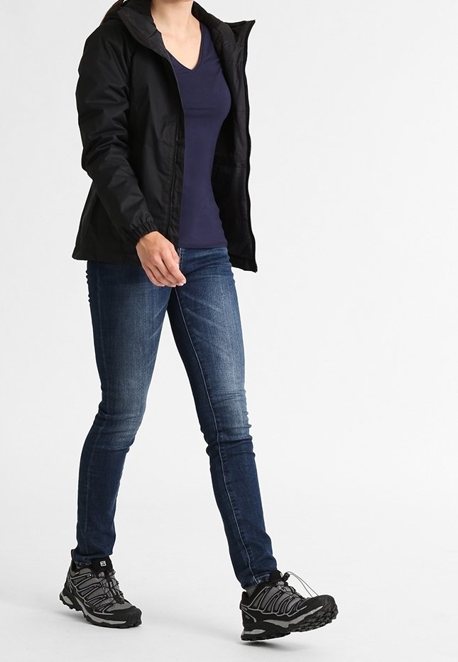 Svart jacka med huva, marinblå V-ringad t-shirt, blå jeans och grå vandringsskor med svarta detaljer, gående på en neutral bakgrund.