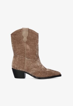 Botas de vaquero de ante marrón con puntas afiladas y tachuelas decorativas de bronce en la parte inferior. Presentan un tacón negro bajo y detalles de costura.