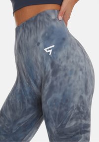 Högmidjade leggings i ett blått tie-dye-mönster, tillverkade av ett slätt, stretchigt material, med en vit logodetalj vid höften.