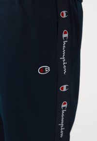 Pantalon bleu marine avec logos de la marque Champion et script le long de la bande latérale et près de la poche.