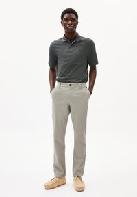 Polo shirt verde scuro a maniche corte, pantaloni beige chiaro e scarpe mocassino color cammello; design semplice con bottone e tasche.