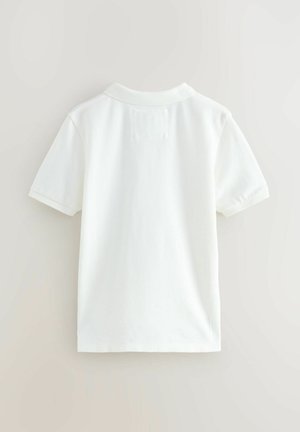 Weißes Poloshirt mit kurzen Ärmeln, flachem Kragen und strukturiertem Stoff. Mit einem kleinen Patchdetail auf dem oberen Rücken.