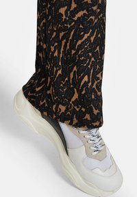 Teniska s vrstveným designem, která kombinuje béžové, bílé a černé materiály. Svršek má směs síťoviny a hladkých textur, s tkaničkami.