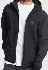 Giacca softshell nera con cappuccio, zip frontale, due tasche laterali e logo ricamato sul petto. Tessuto morbido, vestibilità moderna.