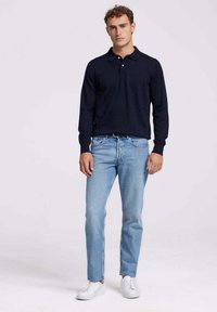 Marineblauw poloshirt met lange mouwen, gecombineerd met lichtblauwe jeans en witte sneakers. Heeft een klassieke kraag en een knoopsluiting.