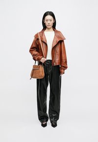 Veste en cuir marron avec grand col, pull crème et pantalon en simili cuir noir. Tenue d'un petit sac en daim beige. Chaussures noires à bouts pointus.