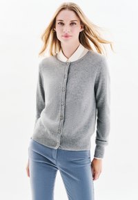 Cardigan grigio realizzato in morbido tessuto, con scollo rotondo, bottoni frontali e polsini a coste. Indossato su una camicia bianca con colletto.
