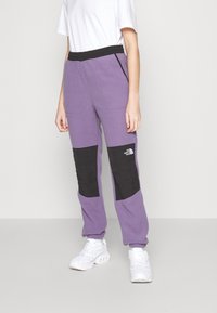 Lila fleecebyxor med svarta knäpatchar, svart elastiskt midjeband och sidofickor. Bärs med vita sneakers.