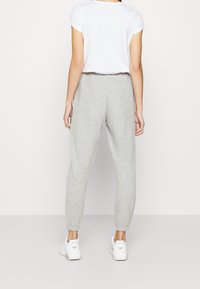 Harmaat trikoot, joissa on joustavat hihnat ja vyötärö, yhdistetty valkoiseen lyhythihaiseen paitaan. Valkoiset tennarit täydentävät asukokonaisuuden.