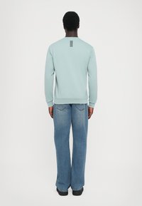 Hanorac de culoare albastru deschis, cu manșete și tiv ribbate, prezentând un detaliu vertical cu dungi negre pe spate. Purtați cu blugi din denim, cu tăietură largă.