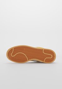 Sole of a sneaker featuring a herringbone pattern in light brown rubber with a smooth gray upper portion and a yellow accent.