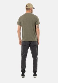 T-shirt vert olive à manches courtes avec un col rond, associé à un pantalon gris foncé et des baskets montantes noires, vu de dos.