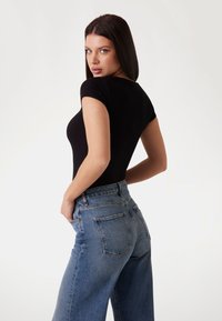 Svart ribbet body med korte ermer, kombinert med høyhåndte blå denimjeans. Har en rett benklipp og baklommer.