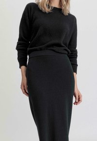 Musta neulepaita pyöreällä kaula-aukolla ja käännetyillä hihoilla, yhdistettynä kapeaan mustaan midi-hameeseen, molemmat pehmeästä, teksturoidusta kankaasta.