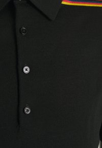 Czarna koszulka polo wykonana z miękkiej tkaniny, z zamkiem na trzy guziki oraz kołnierzykiem z wielokolorowymi paskami wzdłuż szyi.