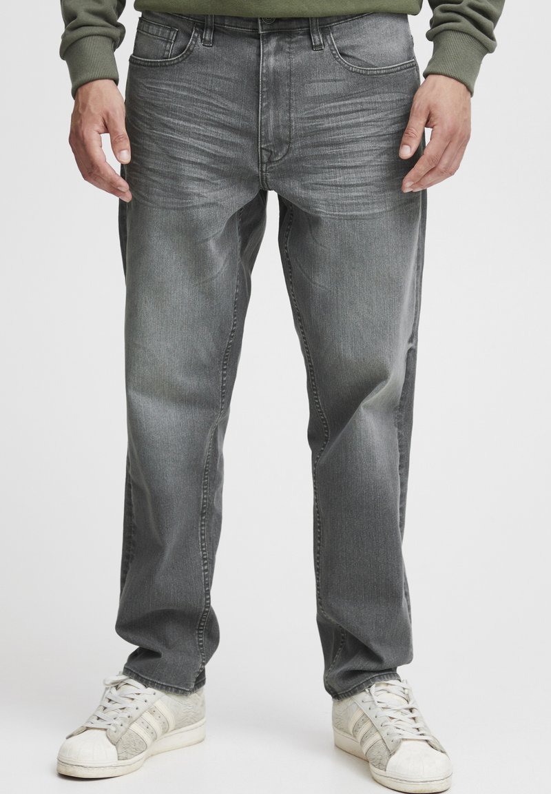 Jeans din denim gri pentru bărbați, cu un croi drept, având o ușoară decolorare, cinci buzunare și închidere cu fermoar. Purtați cu adidași albi.