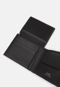 Must musträst nahkrahakott, millel on mitu kaardipesa, tekstureeritud sisemus ja müntide jaoks eraldi tasku. Omab reljeefset "GUESS GENUINE LEATHER" logo.