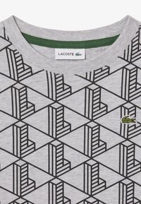 T-shirt grigio con un motivo geometrico nero composto da forme rettangolari. Include un piccolo logo verde ricamato di Lacoste sul petto.
