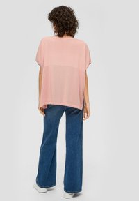 Top rosa lavorato a maglia con maniche corte, dotato di un motivo testurizzato sul retro, abbinato a jeans svasati azzurri chiari e sneakers bianche.