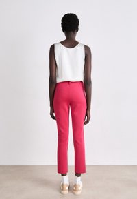 Aangesloten roze broek met een gladde textuur en een iets cropped lengte, gecombineerd met een witte mouwloze top. Zichtbare achternaad en tailleband.