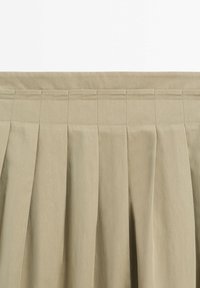 Ceinture de jupe plissée beige avec des coutures verticales et des motifs rectangulaires cousus le long du bord supérieur sur un tissu doux.