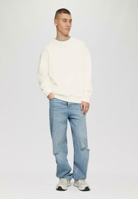 Biała bluza z okrągłym dekoltem, jasnoniebieskie dżinsy z postrzępionymi detalami oraz szaro-białe sneakersy. Casualowy styl, miękka tekstura, luźny fason.