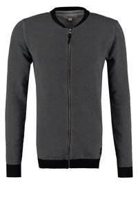 Svart och vit stickad cardigan med rund hals, dragkedja fram, ribbade manschetter och små prickar genom tyget.