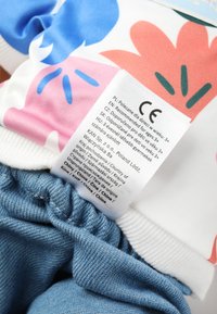 Chemise en coton à imprimé floral rose et bleu, associée à un short en jean avec une ceinture élastique. Étiquette d'entretien visible sur la chemise.