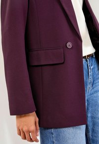 Lilla blazer lavet af glat stof, skræddersyet pasform, enkeltknaplukning og en klaplomme. Matcher med lyseblå denimjeans.