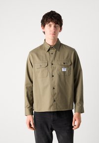 Olive green long-sleeve shirt with button-down collar, two chest pockets, and black buttons, made of a durable cotton blend.