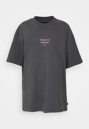 Mørkegrå oversized T-skjorte laget av bomull, med "PREMIUM STUDIOS" i rosa bokstaver på fronten. Korte ermer, rund hals.