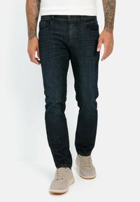 Donkerblauwe denim jeans met een slim fit, voorzien van voorzakken, achterzakken en een enkele knoopsluiting. Gekleed met lichtbeige sneakers.