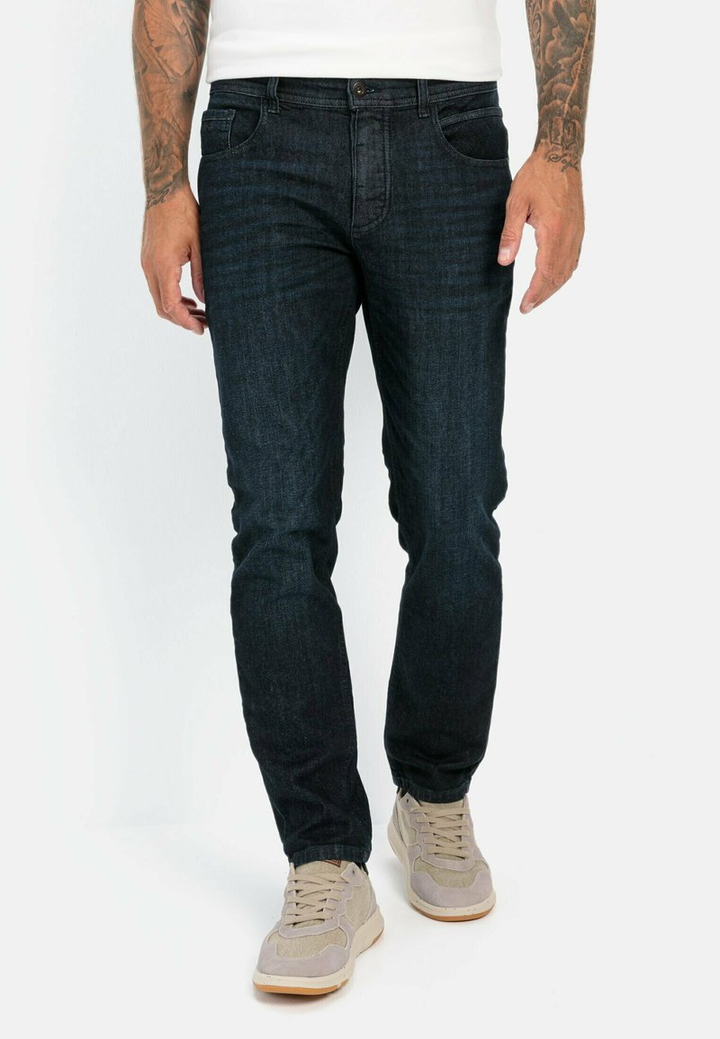 Donkerblauwe denim jeans met een slim fit, voorzien van voorzakken, achterzakken en een enkele knoopsluiting. Gekleed met lichtbeige sneakers.