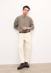 Suéter gris texturizado, pantalones de pierna ancha color crema, cinturón de cuero marrón y botas de tobillo marrón oscuro. Los accesorios incluyen un reloj de plata.