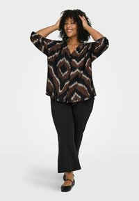 Smeđa i crna bluzica sa uzorkom, V izrezom, dugim rukavima i detaljima s dugmadima, uparena s crnim hlačama i cipelama. Kovrčava kosa je stilizirana.