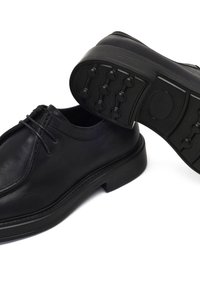 Scarpe in pelle nera con punta arrotondata, design minimale dei lacci e suola in gomma nera testurizzata con grip circolari e bordo rialzato.