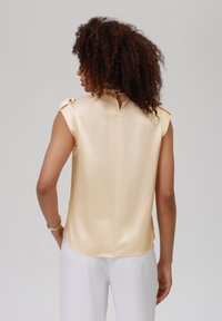 Satin, ärmlös blus i ljusgul med knappdetaljer på axlarna och nyckelhål på baksidan, med en mjuk textur och avslappnad passform.