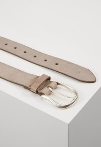 Brauner Leder Gürtel mit glatter Textur, ausgestattet mit mehreren Einstelllöchern und einer silbernen Metallschnalle. Auf einer weißen Oberfläche platziert.