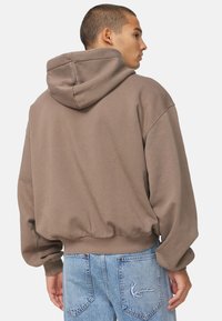 Marokkaanse hoodie met een trekkoordkap, geribbelde onderrand en een oversized pasvorm; gedragen met blauwe denim jeans met geborduurde details op de achterzak.