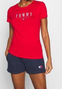 Czerwony bawełniany t-shirt z białym logo "TOMMY JEANS", w połączeniu z granatowymi szortami z małą łatką z logo. Krótkie rękawy i klasyczny krój.