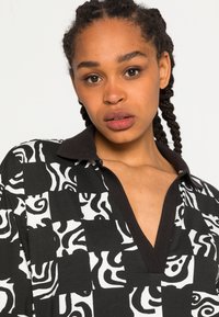 Camisa com padrão preto e branco apresentando designs geométricos e abstratos, com um colarinho escuro e decote em V. Feita de um tecido suave.