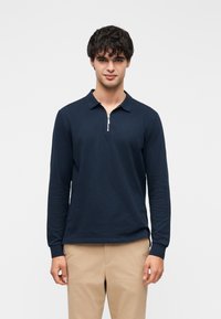 Marineblå langærmet polo med lynlåslukning ved kraven, lavet af blødt bomuldsstof. Veltilpasset design med manchetter ved håndleddene og en glat tekstur.