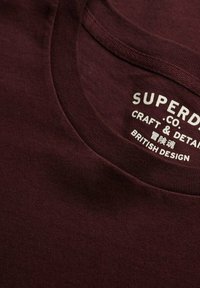 Bordeaux katoenen T-shirt met een ronde hals, voorzien van een zachte textuur, en een bedrukt label met "Superdry" en "British Design".