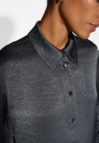 Camicia nera stropicciata con colletto strutturato, dotata di chiusura con bottoni e tessuto testurizzato che offre un dettaglio di superficie unico.