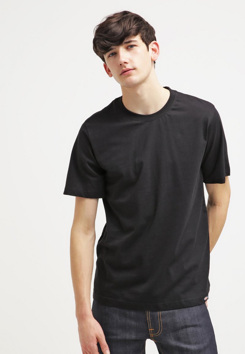 T-shirt nera in cotone con maniche corte, scollatura rotonda e trama liscia. Abbinata a jeans in denim scuro con cuciture arancioni.