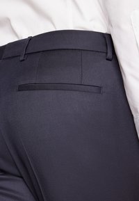 Dark navy formal trousers with a smooth fabric texture, featuring a slim fit, waistband, and a single back pocket with an elegant piping detail.