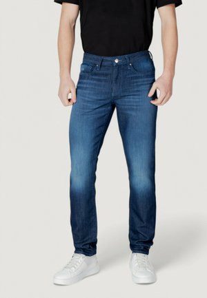 Jeans in denim blu con un taglio dritto, dettagli sbiaditi, stile a cinque tasche e chiusura con bottone metallico, abbinati a sneakers bianche.