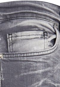 Jeans in denim di colore nero sbiadito, con una tasca posteriore, cuciture rinforzate e un dettaglio del bottone argentato. Tessuto testurizzato con un aspetto consumato.