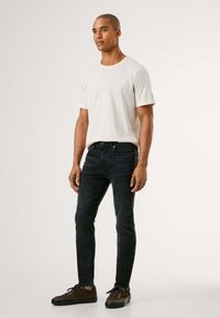 Vaaleanbeige lyhythihainen t-paita, tummansiniset slim fit -farkut, ruskeat lenkkarit, ja sileä, minimalistinen muotoilu ilman näkyviä kuvioita.